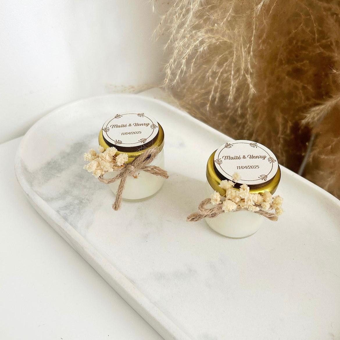 Bougie cadeau invité Blanchette avec couvercle doré, nœud en ficelle et fleurs séchées, personnalisée avec prénoms et date.