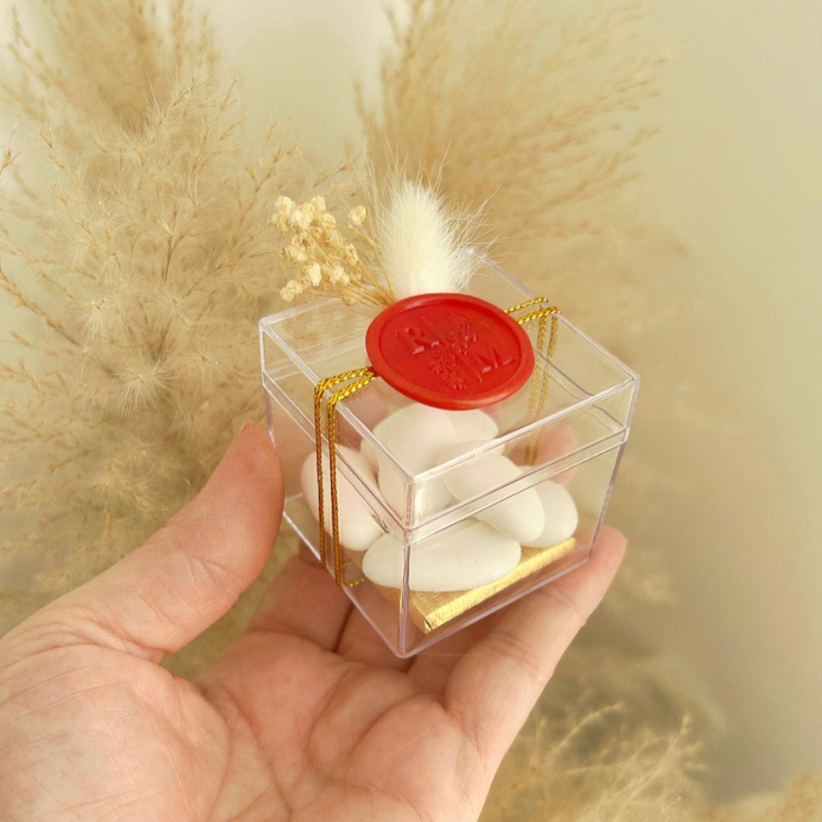 Cadeau invité : boîte de dragées Séduction en plexi avec sceau de cire rouge, ficelle dorée et décoration florale.