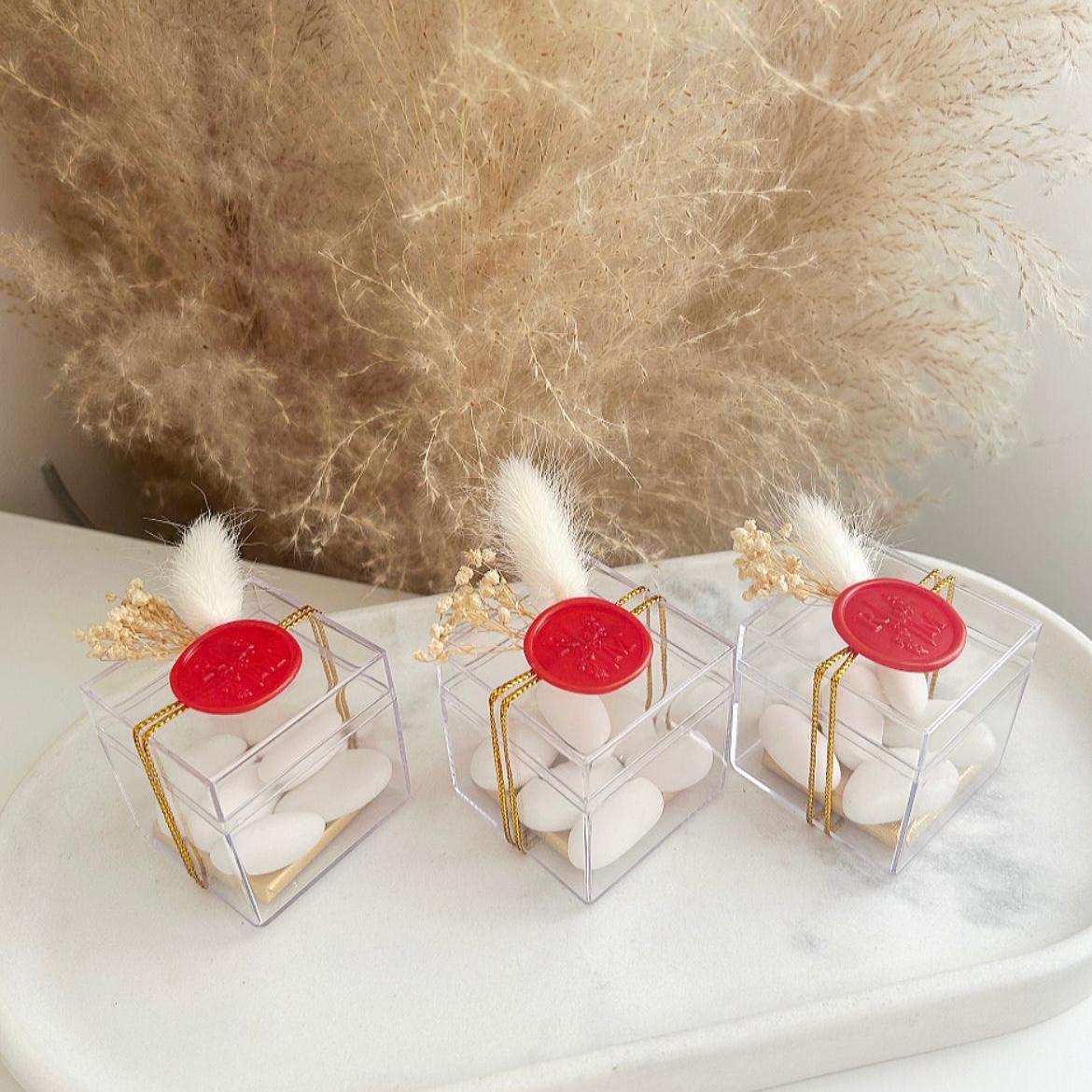 Cadeau invité : boîte de dragées Séduction en plexi avec sceau de cire rouge, ficelle dorée et décoration florale.