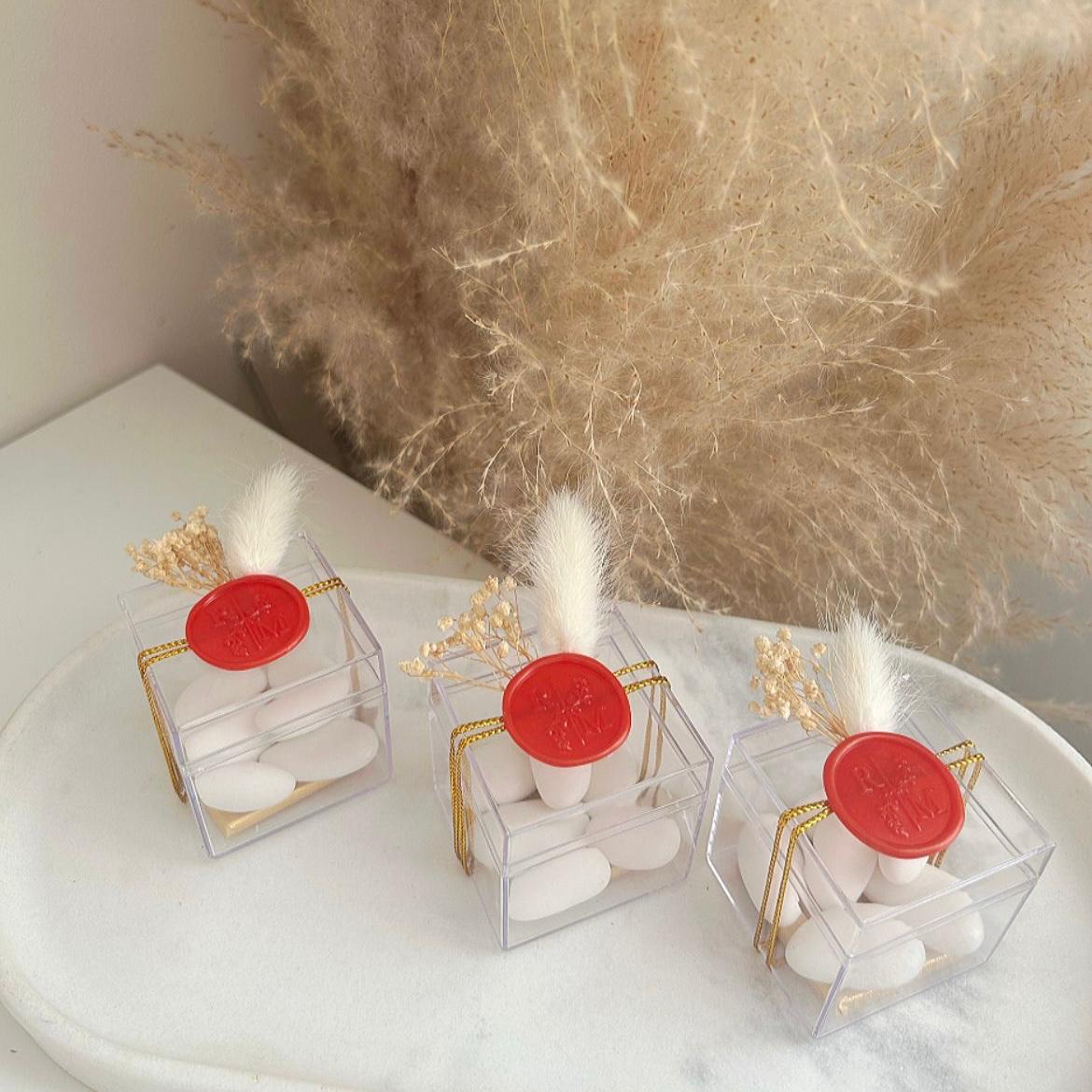 Cadeau invité : boîte de dragées Séduction en plexi avec sceau de cire rouge, ficelle dorée et décoration florale.