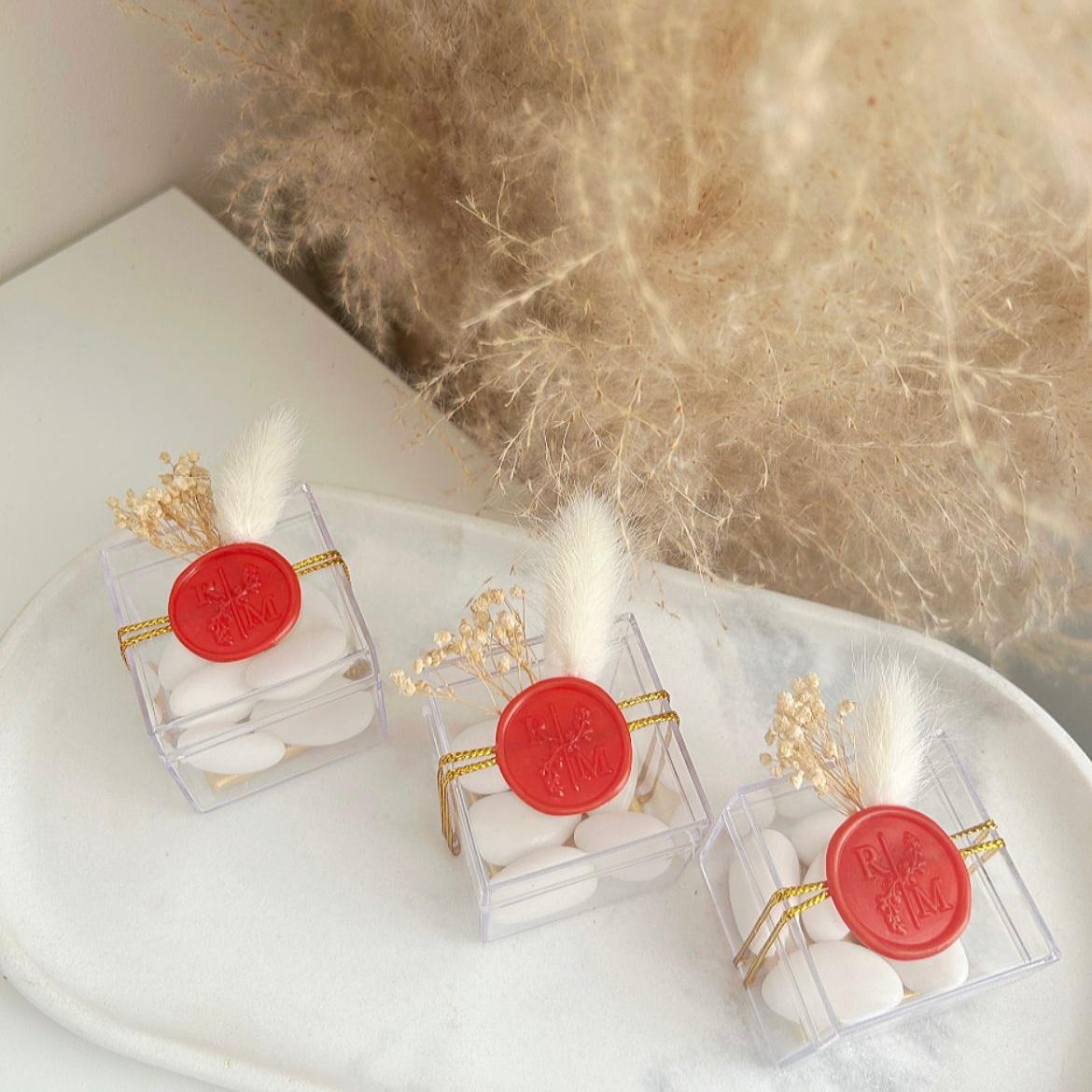 Cadeau invité : boîte de dragées Séduction en plexi avec sceau de cire rouge, ficelle dorée et décoration florale.