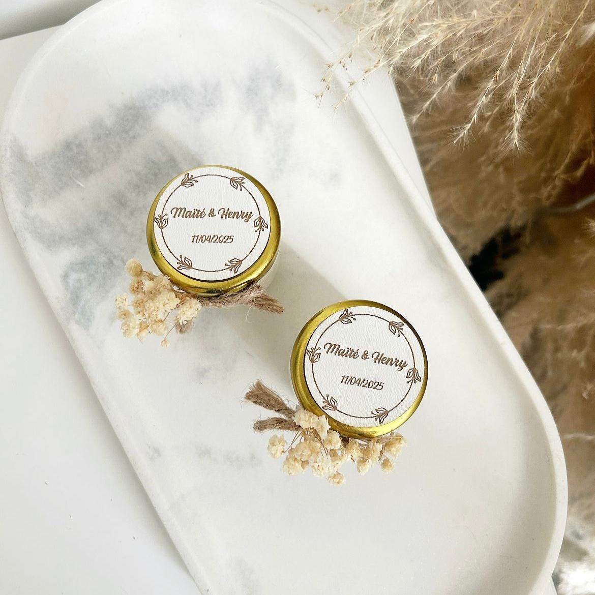 Bougie cadeau invité Blanchette avec couvercle doré, nœud en ficelle et fleurs séchées, personnalisée avec prénoms et date.