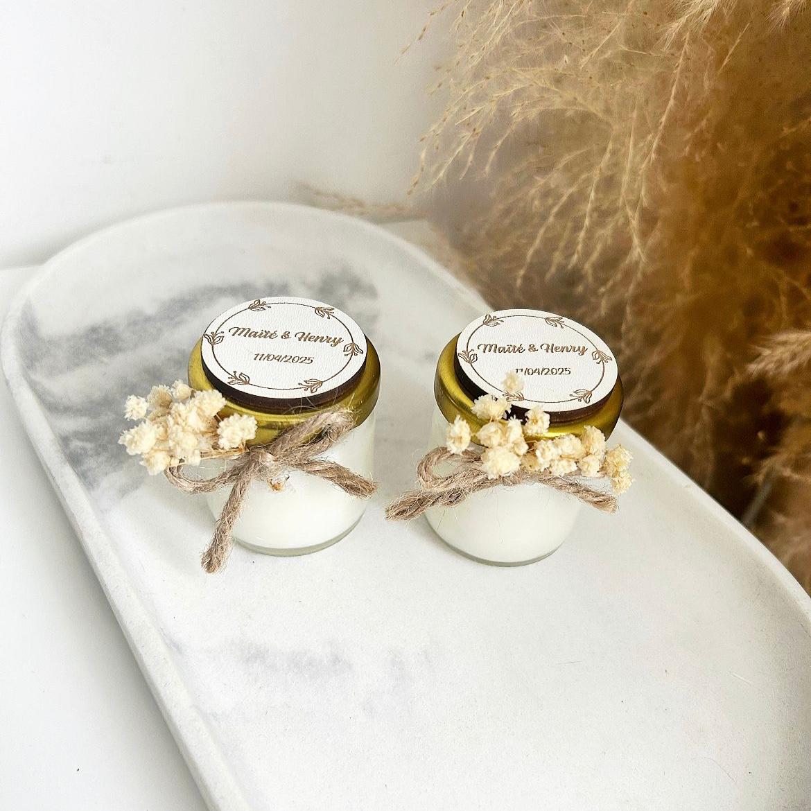 Bougie cadeau invité Blanchette avec couvercle doré, nœud en ficelle et fleurs séchées, personnalisée avec prénoms et date.