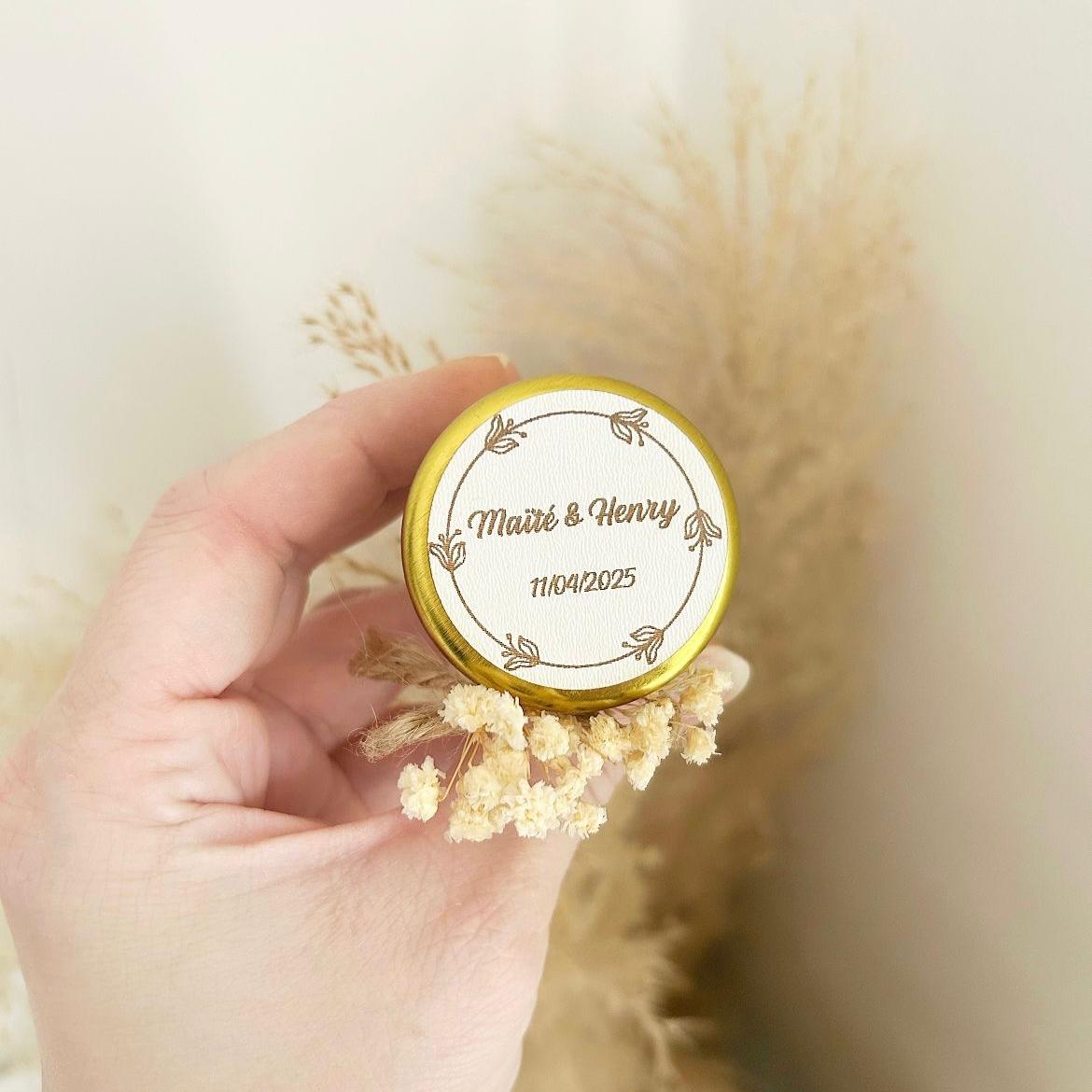 Bougie cadeau invité Blanchette avec couvercle doré, nœud en ficelle et fleurs séchées, personnalisée avec prénoms et date.