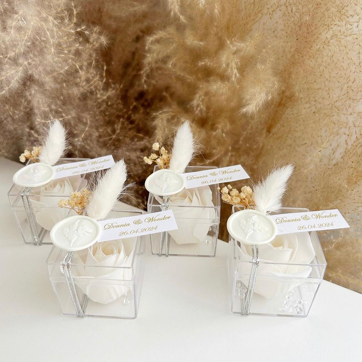Cadeau invité : rose de savon Sisi en boîte plexi avec plume blanche, sceau décoratif et personnalisation des prénoms.