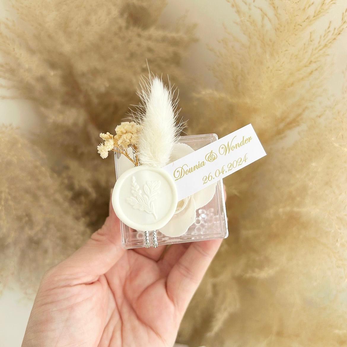 Cadeau invité : rose de savon Sisi en boîte plexi avec plume blanche, sceau décoratif et personnalisation des prénoms.