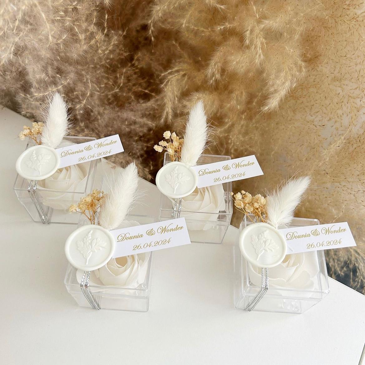 Cadeau invité : rose de savon Sisi en boîte plexi avec plume blanche, sceau décoratif et personnalisation des prénoms.